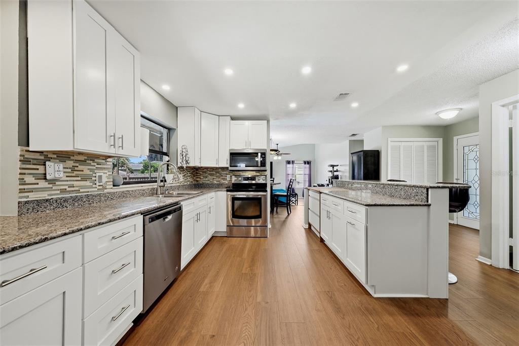 A modern kitchen features white cabinetry, granite countertops, stainless steel appliances, and wood-look flooring — 3916 BLOOMING HILL LANE, PALM HARBOR, FL