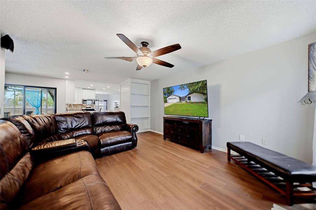 A living room with wood-look flooring, a brown leather sectional, and a wall-mounted television — 3916 BLOOMING HILL LANE, PALM HARBOR, FL