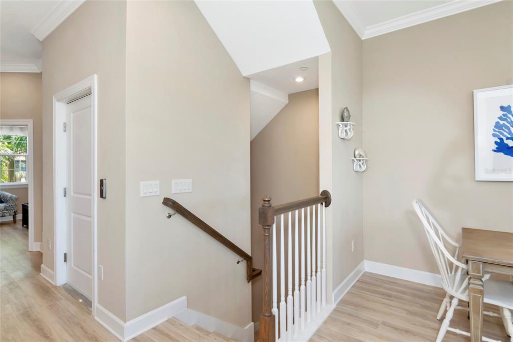 A staircase with a wooden handrail and white balusters leads down from a neutral-toned hallway — 5589 CANNES CIRCLE UNIT 4-102, SARASOTA, FL