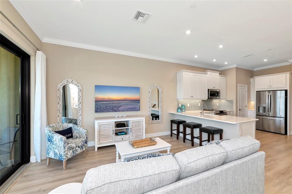 A living room and kitchen area with light wood floors, white cabinetry, and a television — 5589 CANNES CIRCLE UNIT 4-102, SARASOTA, FL