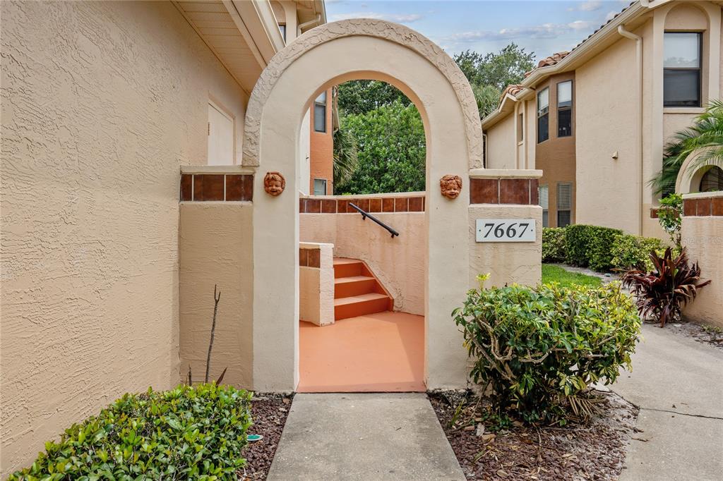 An arched entryway leads to a set of stairs outside a tan stucco building — 7667 SUGAR BEND DRIVE UNIT 7667, ORLANDO, FL
