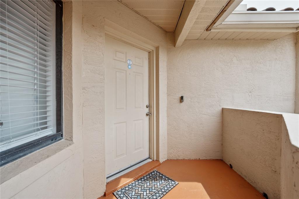 An exterior view of a residential entryway with a beige door and a small porch — 7667 SUGAR BEND DRIVE UNIT 7667, ORLANDO, FL