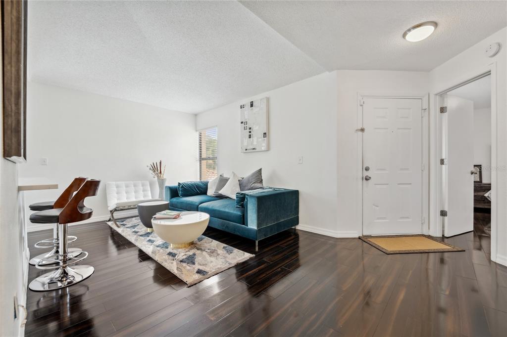 A living room features dark wood floors, a blue velvet sofa, and a white front door — 7667 SUGAR BEND DRIVE UNIT 7667, ORLANDO, FL