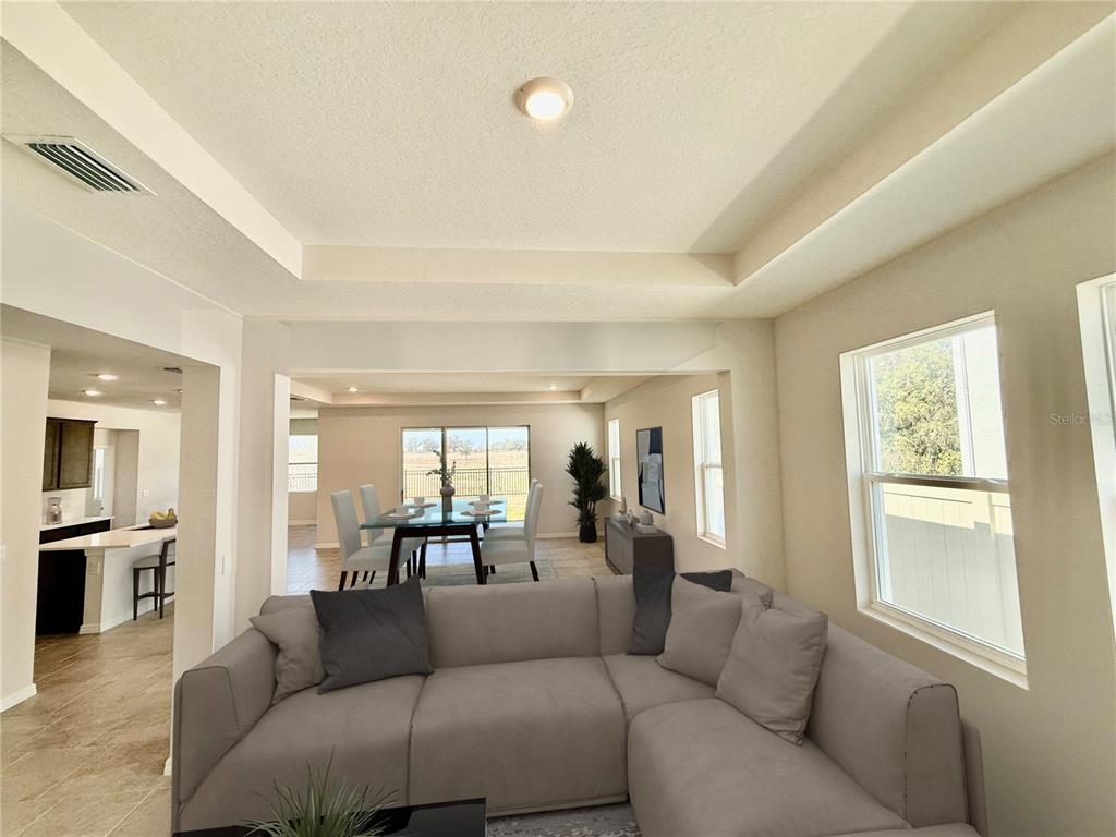 A living room with a sectional sofa opens to a dining area with sliding glass doors — 10471 BRIDGEGATE HEIGHTS LOOP, SAN ANTONIO, FL
