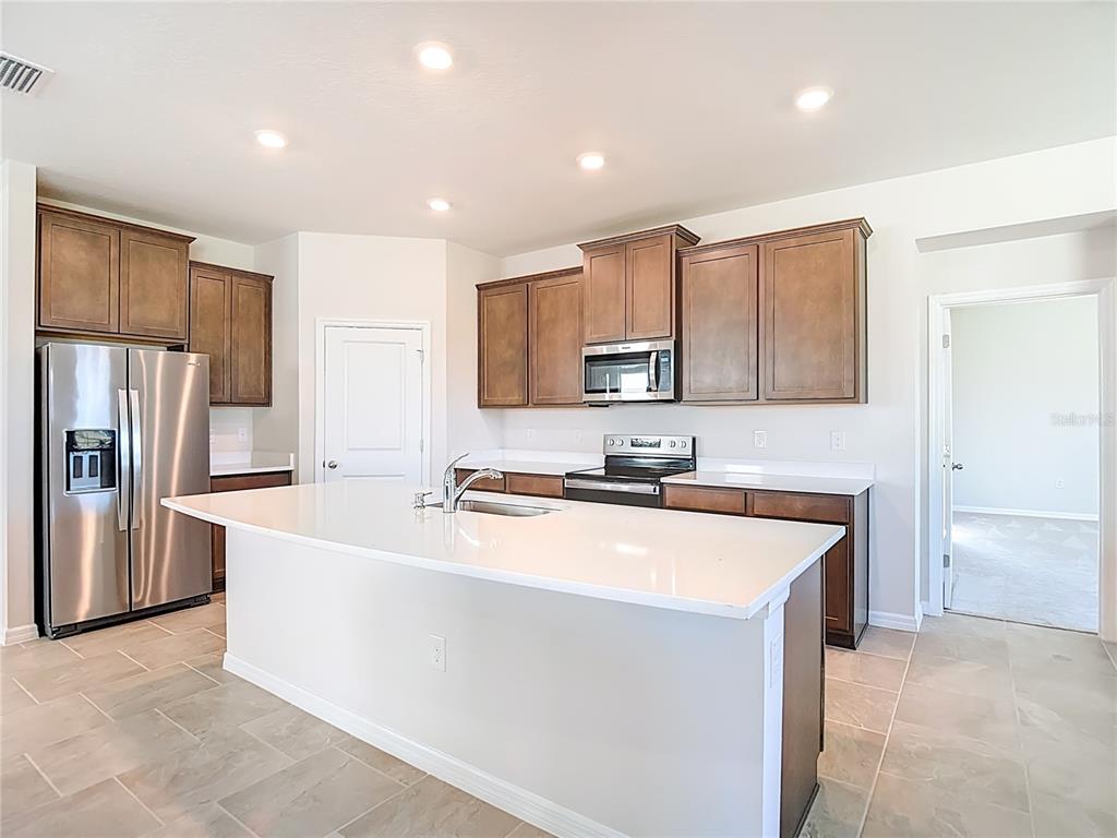 A kitchen features a white island, stainless steel appliances, and dark wood cabinets — 10471 BRIDGEGATE HEIGHTS LOOP, SAN ANTONIO, FL