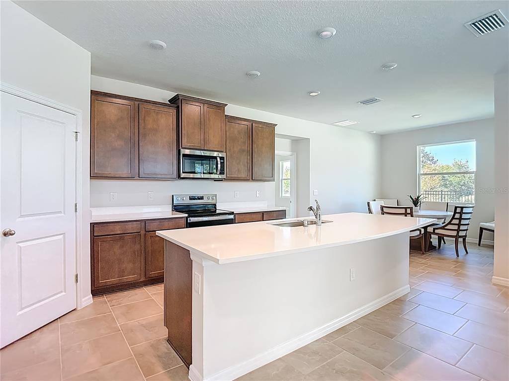 A kitchen features dark wood cabinets, white countertops, a central island, and tile flooring — 10471 BRIDGEGATE HEIGHTS LOOP, SAN ANTONIO, FL