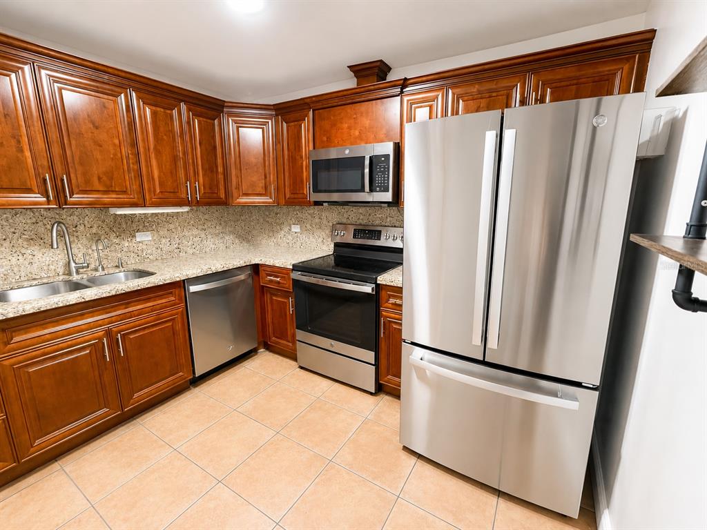 A kitchen features wood cabinets, granite countertops, stainless steel appliances, and light-colored tile flooring — 1201 S OCEAN DRIVE UNIT 314S, HOLLYWOOD, FL