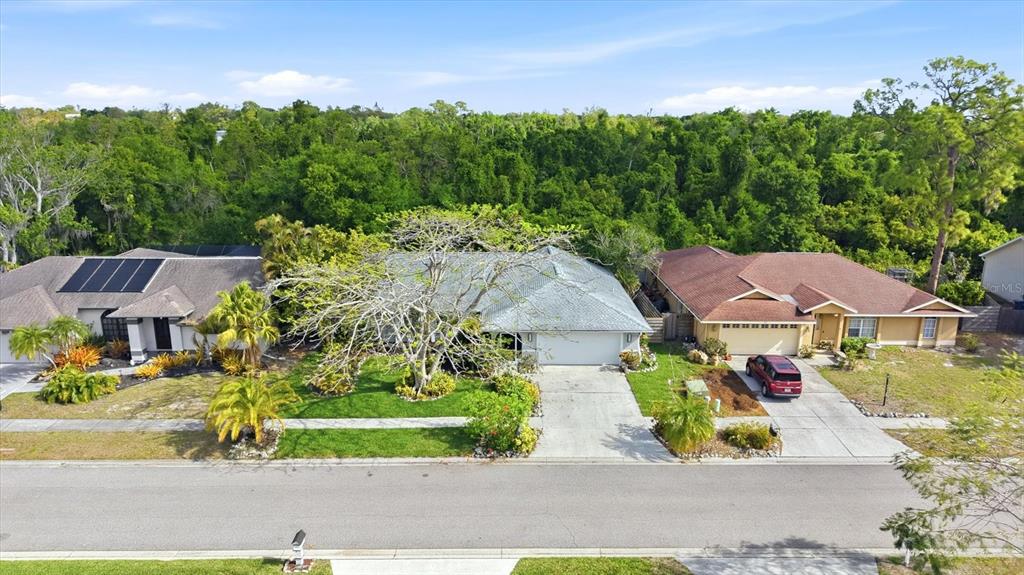 An aerial view shows three suburban houses with driveways and lawns bordering a dense forest — 5599 WILDE OAK WAY, SARASOTA, FL