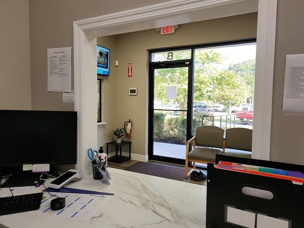 A reception desk overlooks a waiting area with two chairs and an exterior glass door — 3721 S US HIGHWAY 27 UNIT B, CLERMONT, FL