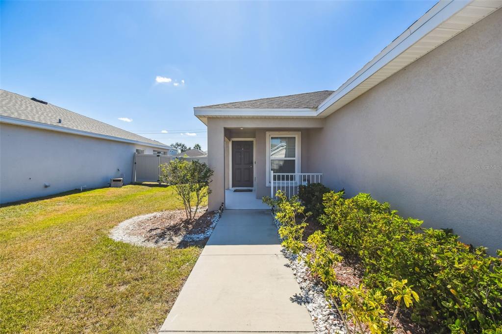A concrete walkway leads to the front entrance of a house with beige stucco siding — 114 EAGLE SUMMIT DRIVE, RUSKIN, FL