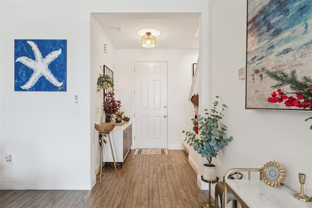 A bright entryway features wood-look tile flooring, a white front door, and coastal-themed wall art — 4395 RENLY LANE, CLERMONT, FL
