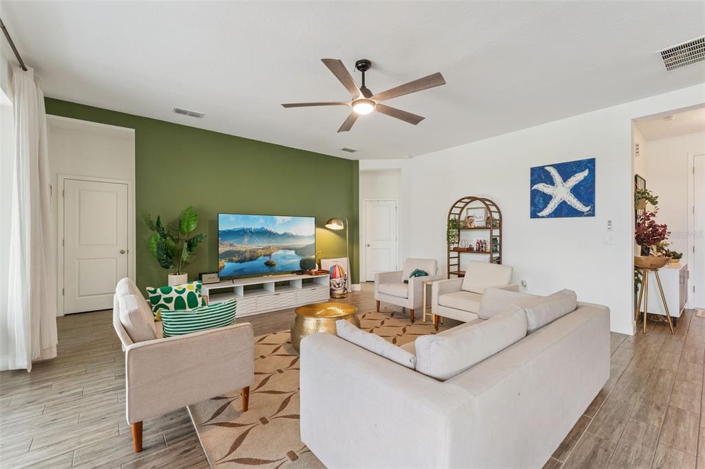 A living room features a green accent wall, a large television, and light-colored furniture — 4395 RENLY LANE, CLERMONT, FL