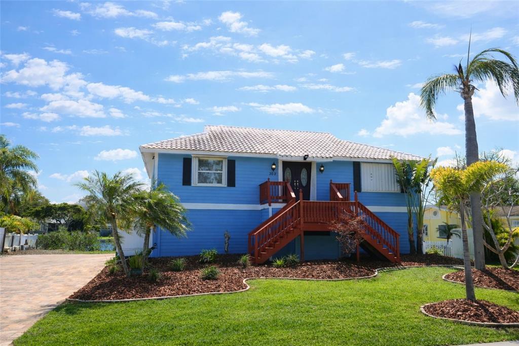 A blue elevated house with a red wooden staircase and a palm tree in front — 303 LAGOON DRIVE, PALM HARBOR, FL