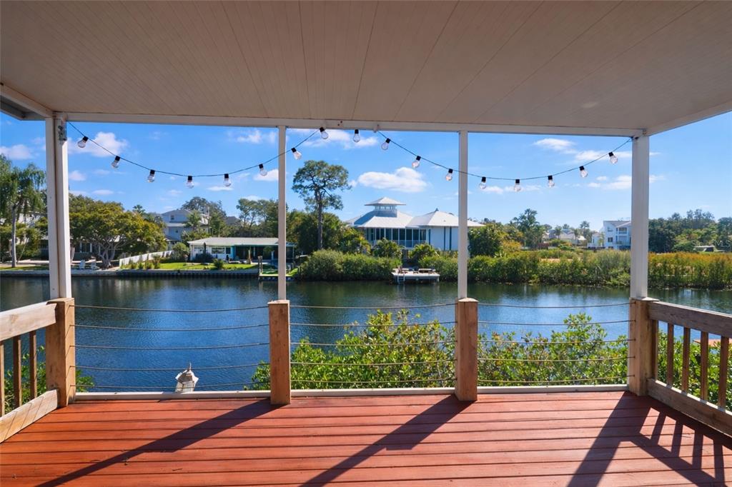 A wooden deck with a cable railing overlooks a canal and houses under a blue sky — 303 LAGOON DRIVE, PALM HARBOR, FL