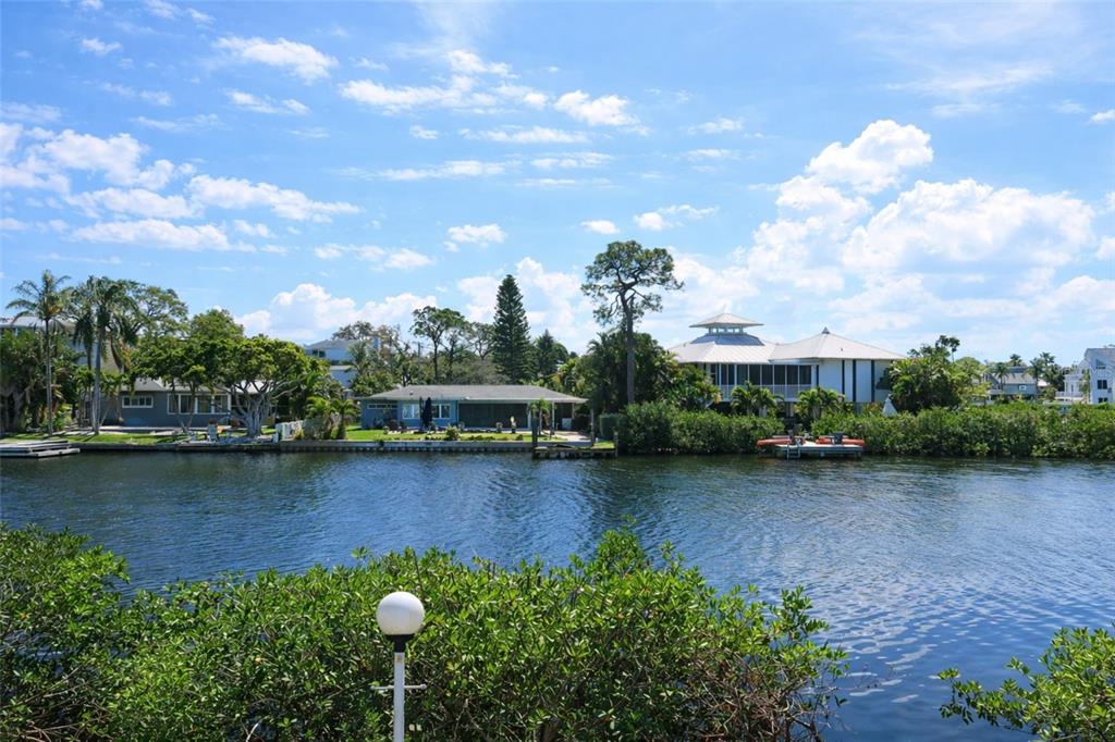 A view of waterfront houses across a canal with lush vegetation and a blue sky — 303 LAGOON DRIVE, PALM HARBOR, FL