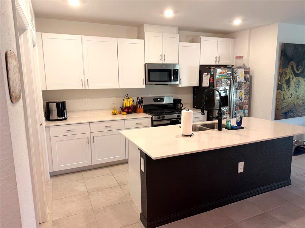 A kitchen features white cabinets, a black island with a white countertop, and stainless appliances — 9116 TEQUILA SUNRISE DRIVE, SARASOTA, FL