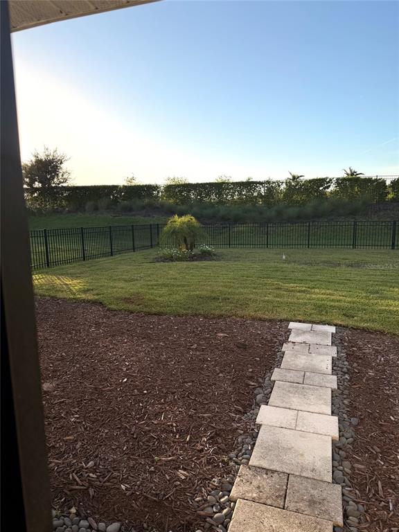 A backyard features a stone paver path, mulch landscaping, a small palm tree, and metal fencing — 9116 TEQUILA SUNRISE DRIVE, SARASOTA, FL