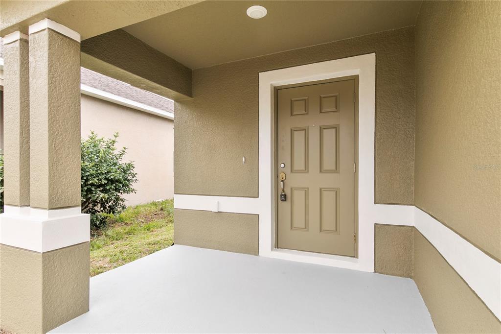 A covered front porch with a tan door, white trim, and a gray concrete floor — 15407 LOST CREEK LANE, RUSKIN, FL