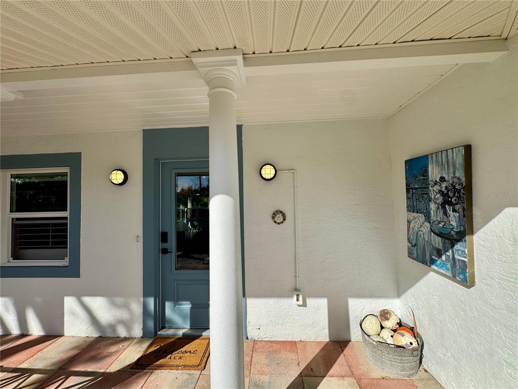 A covered front porch features a white column, a blue door, and a wall-mounted painting — 7372 MELALEUCA WAY, SARASOTA, FL