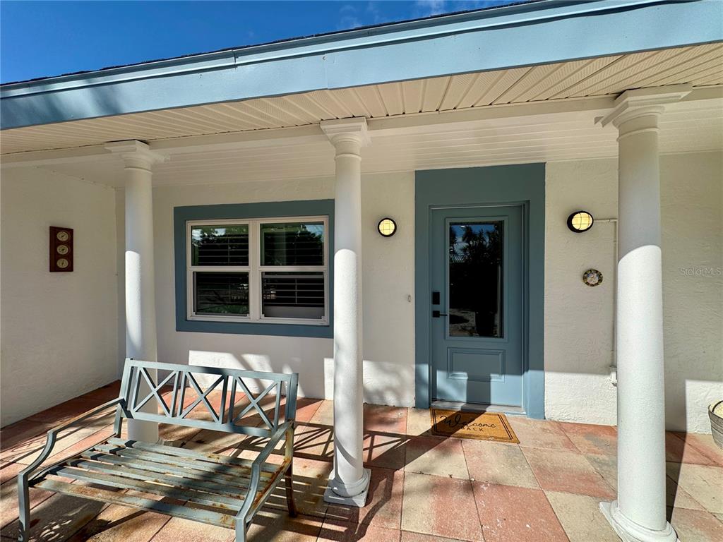 A covered front porch features a metal bench, a blue door, and white columns — 7372 MELALEUCA WAY, SARASOTA, FL