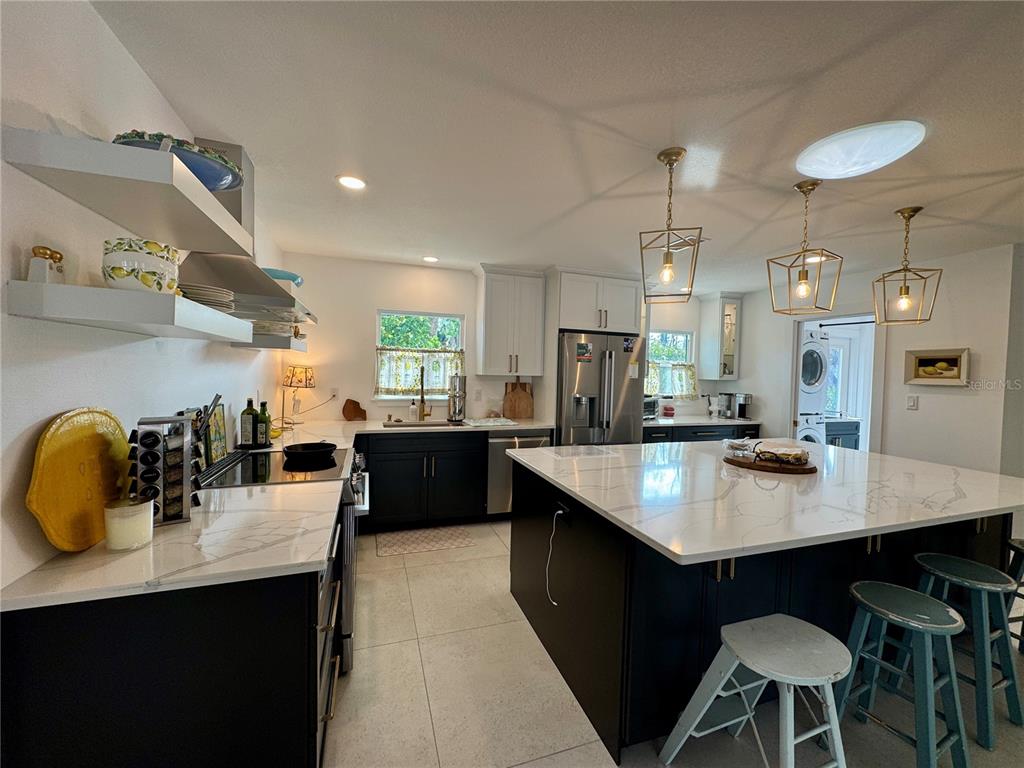 A modern kitchen features dark cabinets, white marble countertops, an island, and three pendant lights — 7372 MELALEUCA WAY, SARASOTA, FL