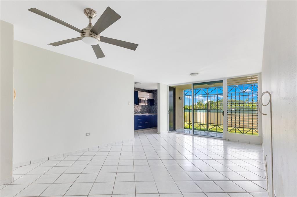 A bright, tiled living area features a ceiling fan, a blue kitchen, and sliding glass doors — AVE. TRIOVEGABAJEÑO COND. TORRE VISTA APT. 1504, VEGA BAJA, PR