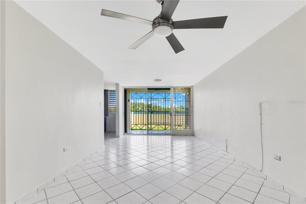 A bright, empty room features white tiled floors, a ceiling fan, and sliding glass doors — AVE. TRIOVEGABAJEÑO COND. TORRE VISTA APT. 1504, VEGA BAJA, PR