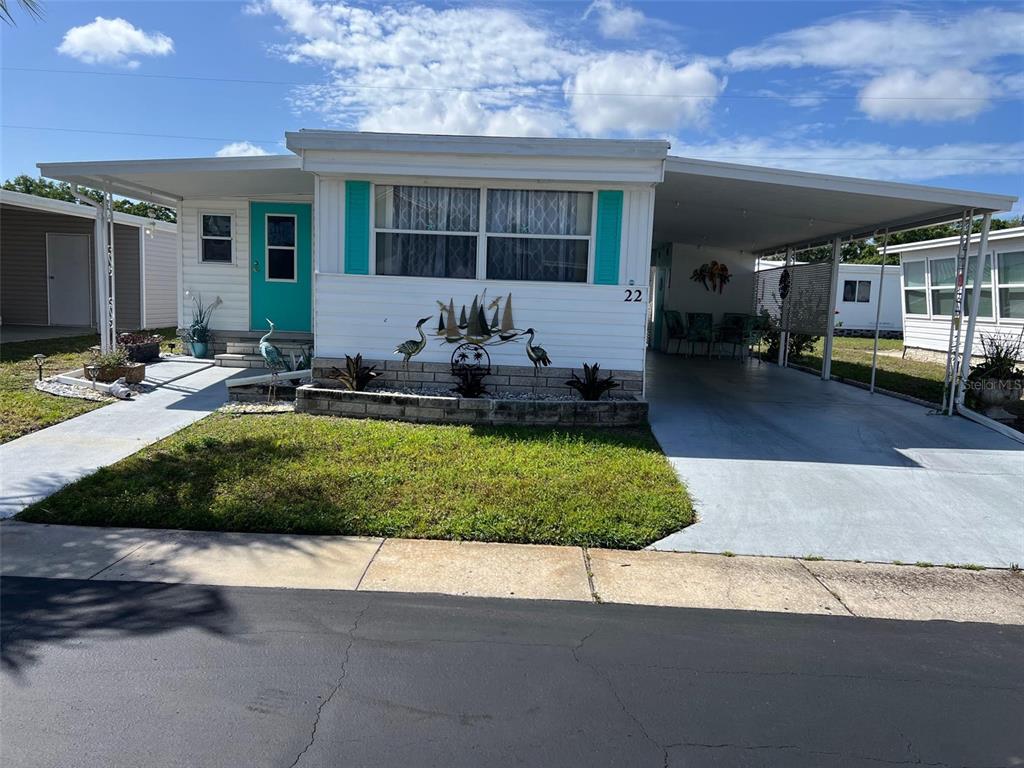 A single-story mobile home features a turquoise front door, a carport, and a landscaped planter — 1500 COUNTY ROAD 1 UNIT 22, DUNEDIN, FL