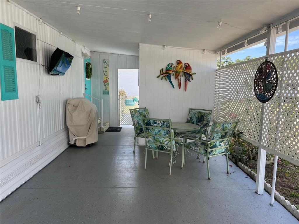A covered patio features a dining set, parrot wall art, and a grill with cover — 1500 COUNTY ROAD 1 UNIT 22, DUNEDIN, FL
