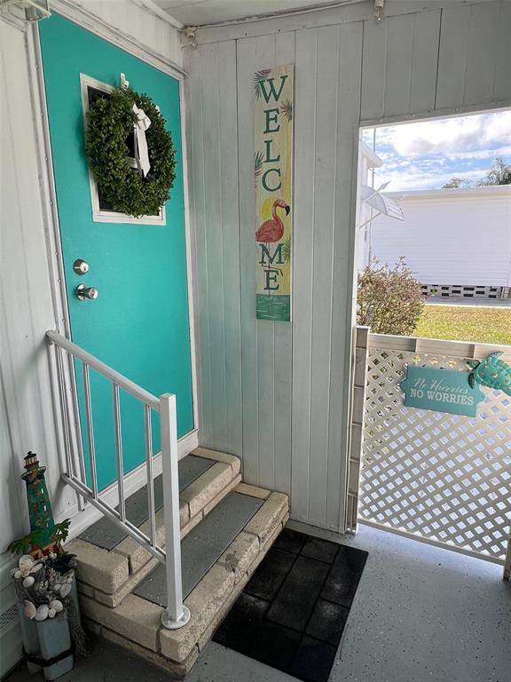 A turquoise front door with a wreath and a welcome sign opens to a porch — 1500 COUNTY ROAD 1 UNIT 22, DUNEDIN, FL