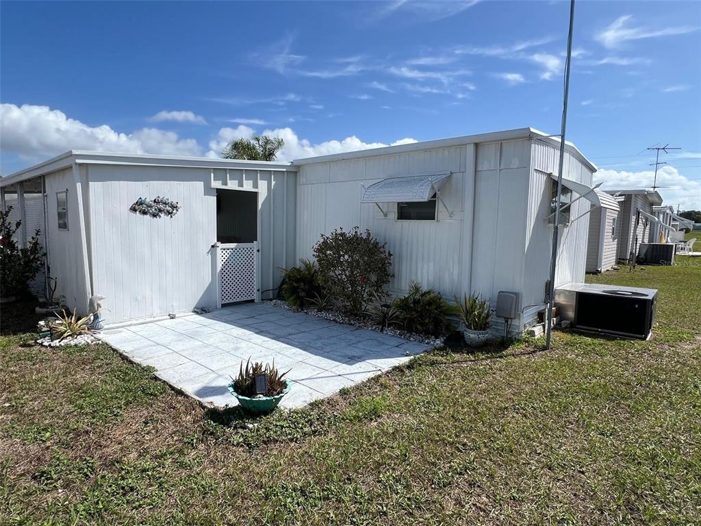 A white mobile home features a paved patio area and a small side entrance — 1500 COUNTY ROAD 1 UNIT 22, DUNEDIN, FL