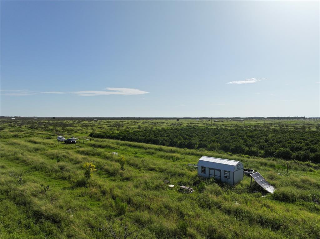 An aerial view shows a small shed with solar panels in a large, grassy field — NE HWY 70, ARCADIA, FL