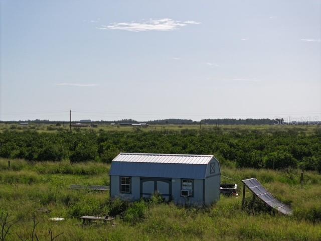 A small shed with a metal roof sits in a grassy field near an orchard — NE HWY 70, ARCADIA, FL
