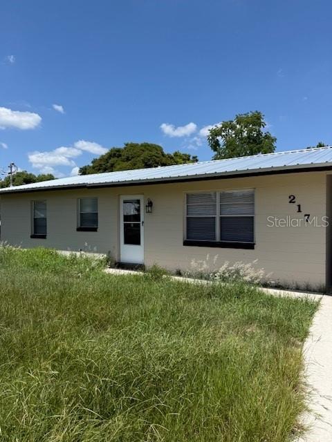 A single-story house with a metal roof and light-colored siding stands behind an overgrown lawn — 217 ALDO DRIVE, BABSON PARK, FL