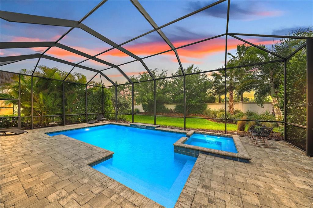 A screened-in swimming pool and spa with a stone patio at sunset — 208 CORELLI DRIVE, NOKOMIS, FL