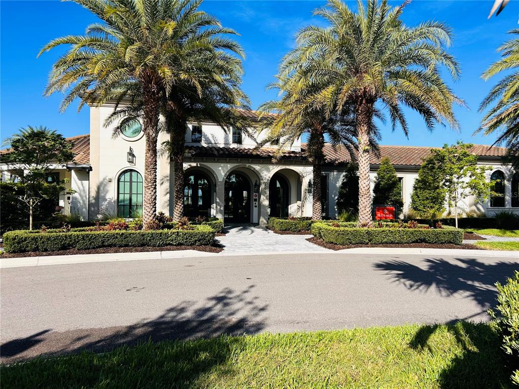 A Mediterranean-style clubhouse exterior features arched entryways, palm trees, and a paved walkway — 208 CORELLI DRIVE, NOKOMIS, FL