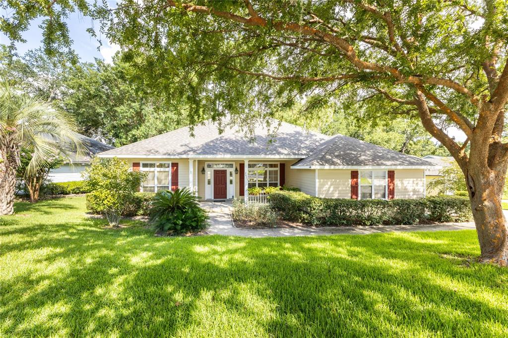 A single-story house with tan siding, red shutters, and a front porch under large trees — 2429 NW 93RD STREET, GAINESVILLE, FL
