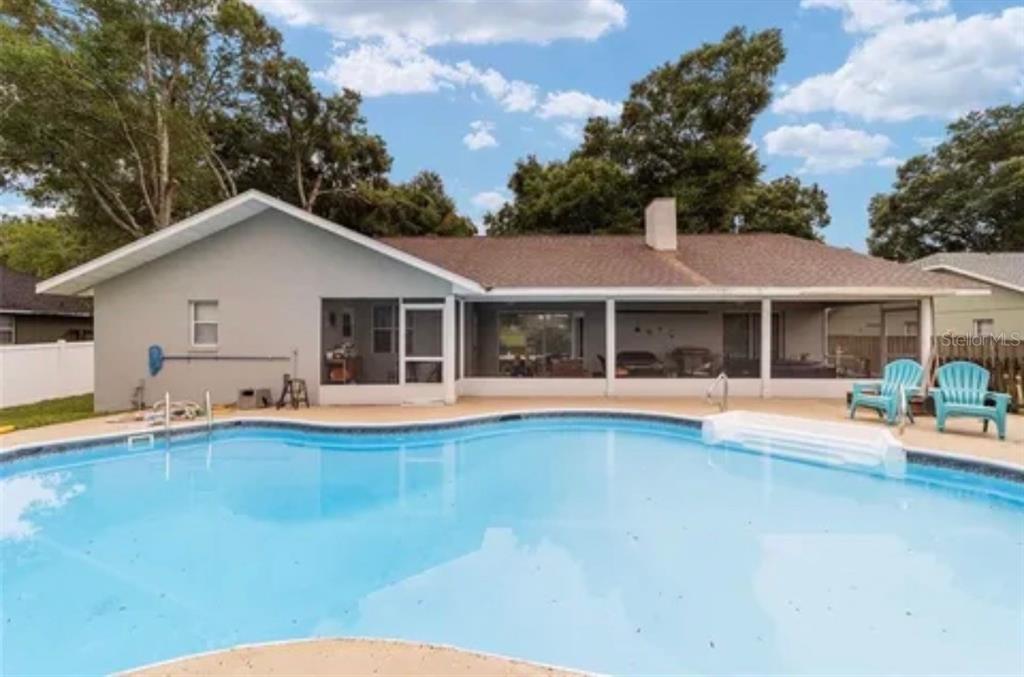 A backyard swimming pool sits in front of a single-story house with a screened-in patio — 3322 SE 55TH COURT, OCALA, FL