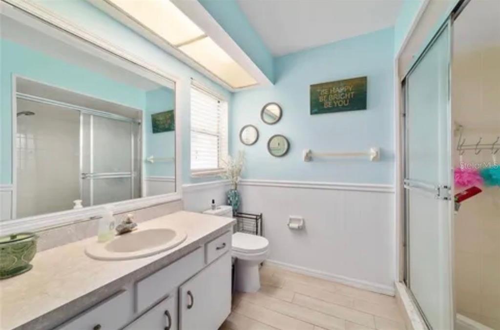 A bathroom with a white vanity, light blue walls, a toilet, and a glass shower enclosure — 3322 SE 55TH COURT, OCALA, FL