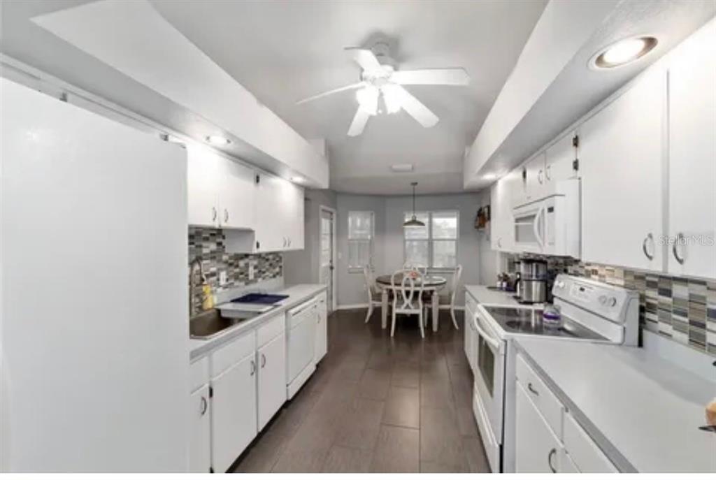 A galley kitchen with white cabinets, stainless steel appliances, and a dining area in the back — 3322 SE 55TH COURT, OCALA, FL