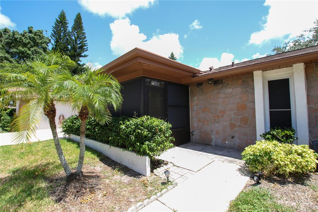 A stone-faced house exterior features a screened-in entryway and a small palm tree — 2360 SHELLY DRIVE UNIT B, PALM HARBOR, FL