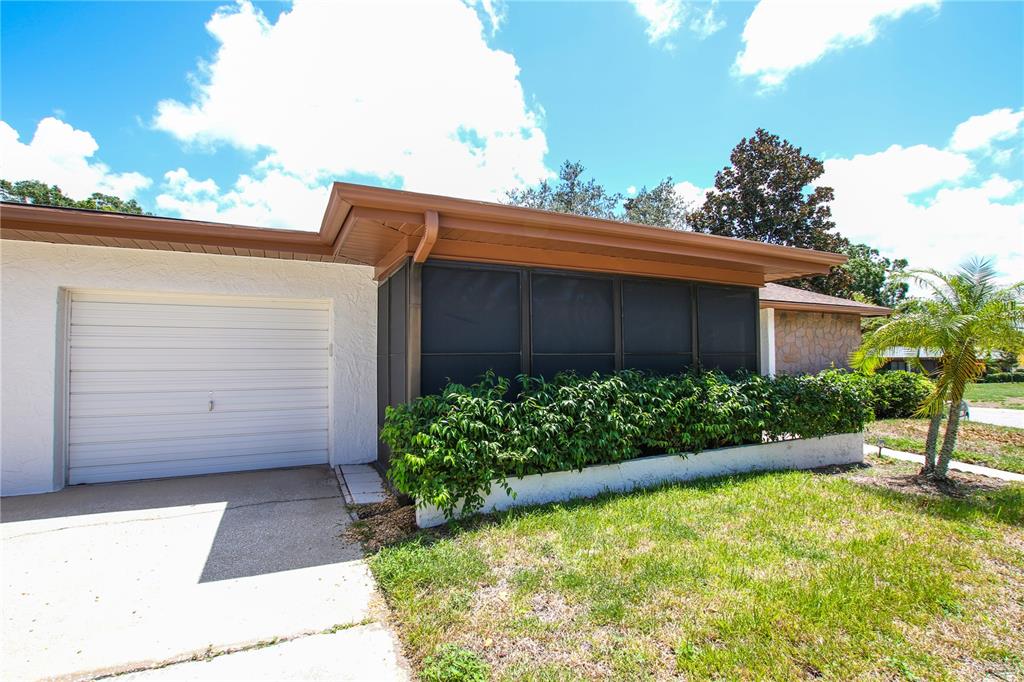 The exterior of a house features a white garage door, a screened-in porch, and landscaping — 2360 SHELLY DRIVE UNIT B, PALM HARBOR, FL