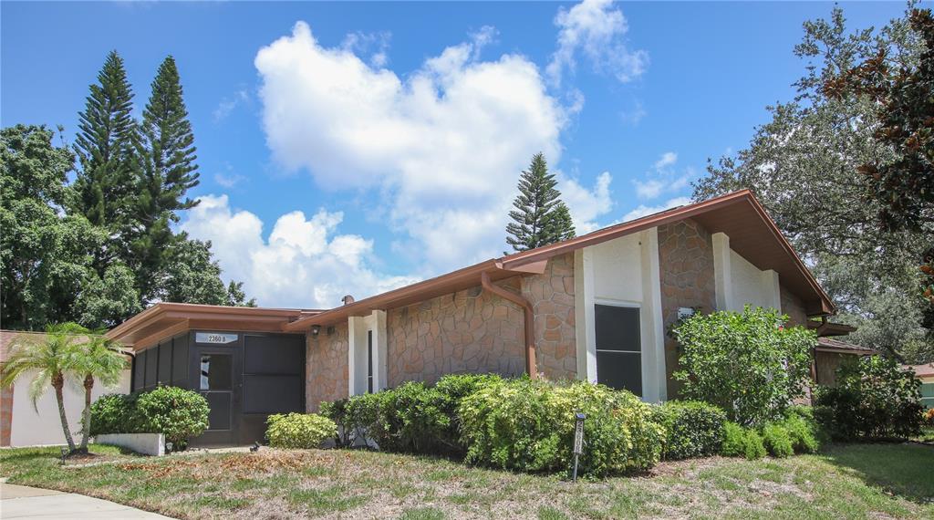 A single-story house with stone veneer siding, a screened-in porch, and a landscaped front yard — 2360 SHELLY DRIVE UNIT B, PALM HARBOR, FL