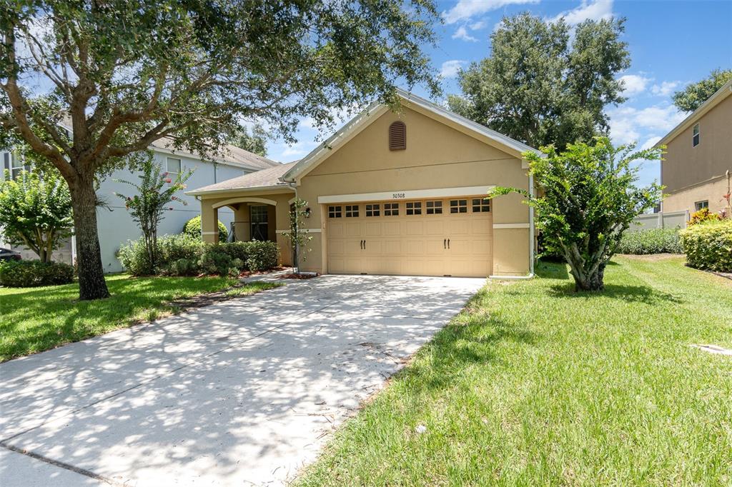 A tan single-story house with a two-car garage and a concrete driveway — 30308 CHEVAL STREET, MOUNT DORA, FL