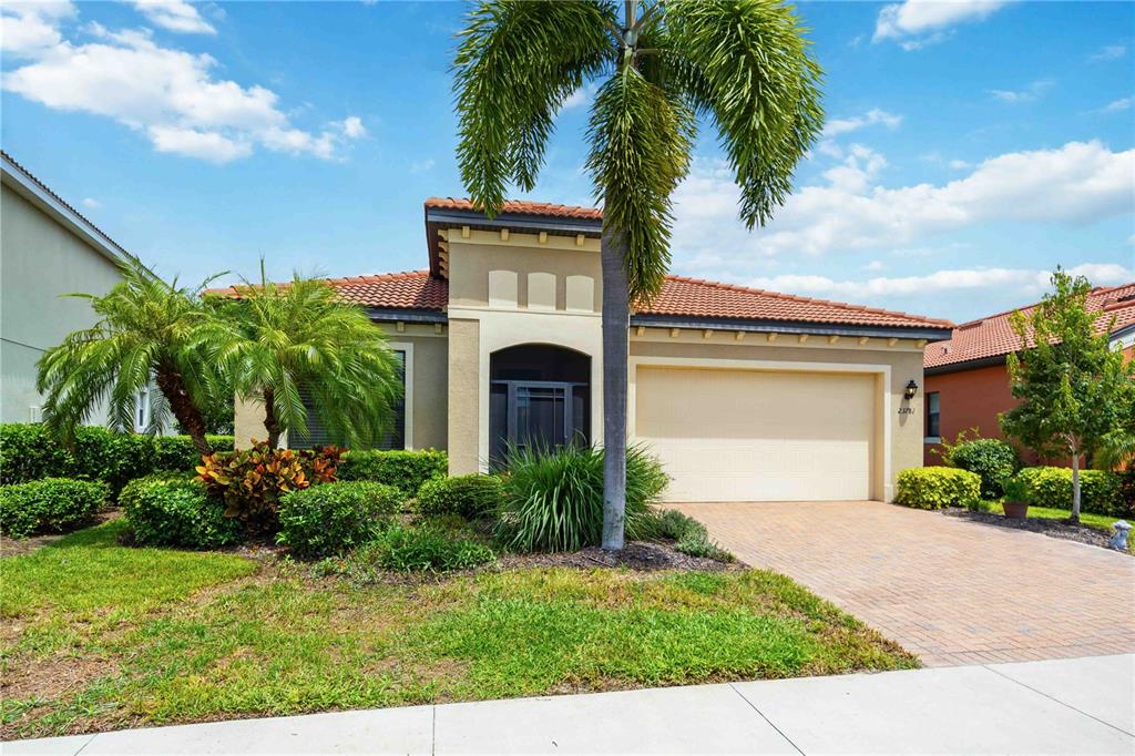 A single-story house with a tan stucco exterior, a tile roof, and a paved driveway — 23781 WAVERLY CIRCLE, VENICE, FL