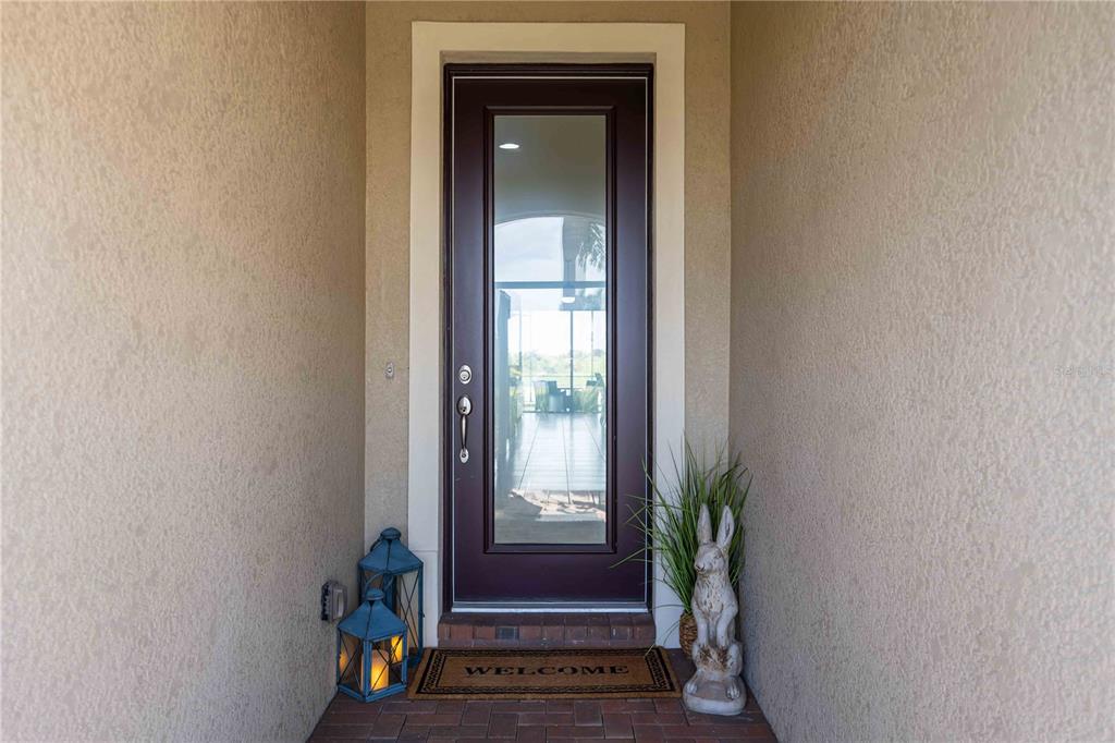 A front door with a glass panel is framed by beige walls and a brick floor — 23781 WAVERLY CIRCLE, VENICE, FL