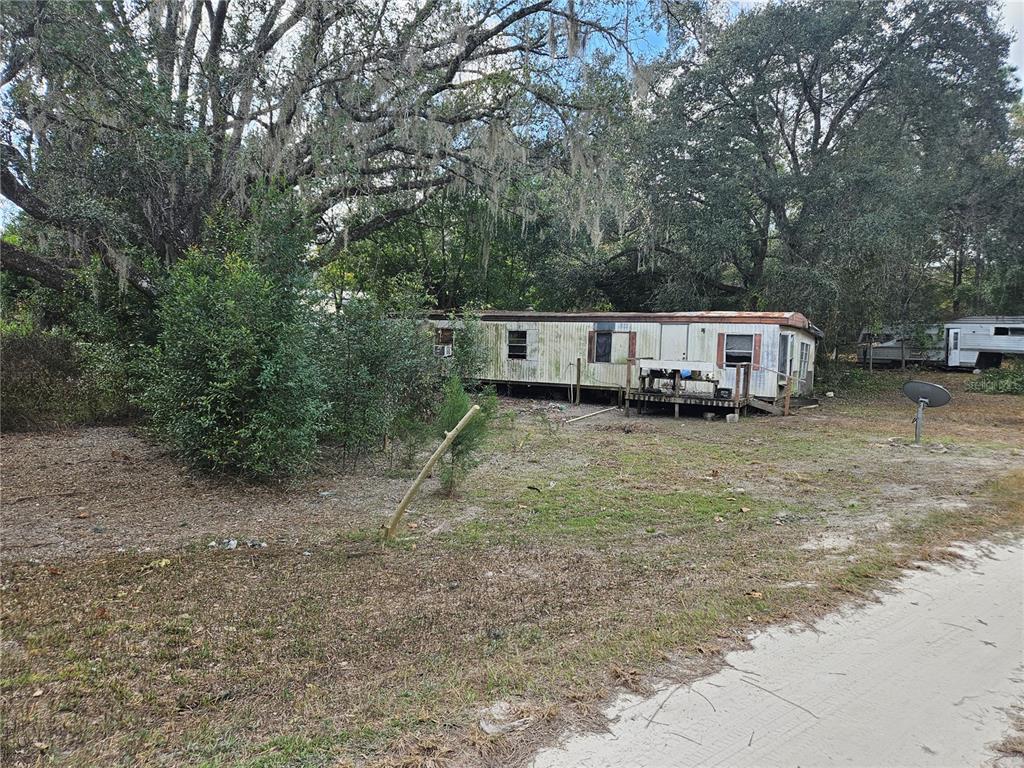 An old, weathered mobile home sits on a grassy lot shaded by large oak trees — 15950 NE 4TH PLACE, WILLISTON, FL