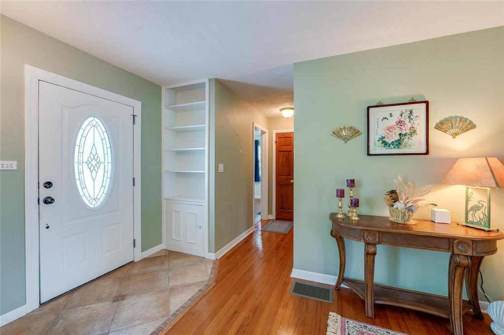 A living room with hardwood floors, a patterned sofa, and an entryway with a white door — 697 JOHN ANDERSON DRIVE, ORMOND BEACH, FL