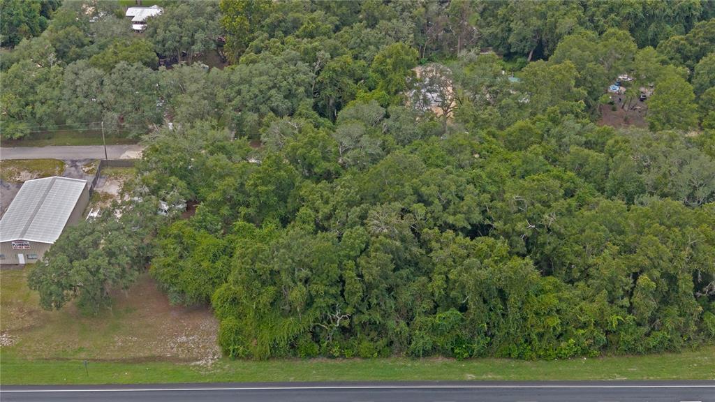 An aerial view shows a densely wooded lot situated between a road and a metal building — 0 N HWY 19, CHIEFLAND, FL
