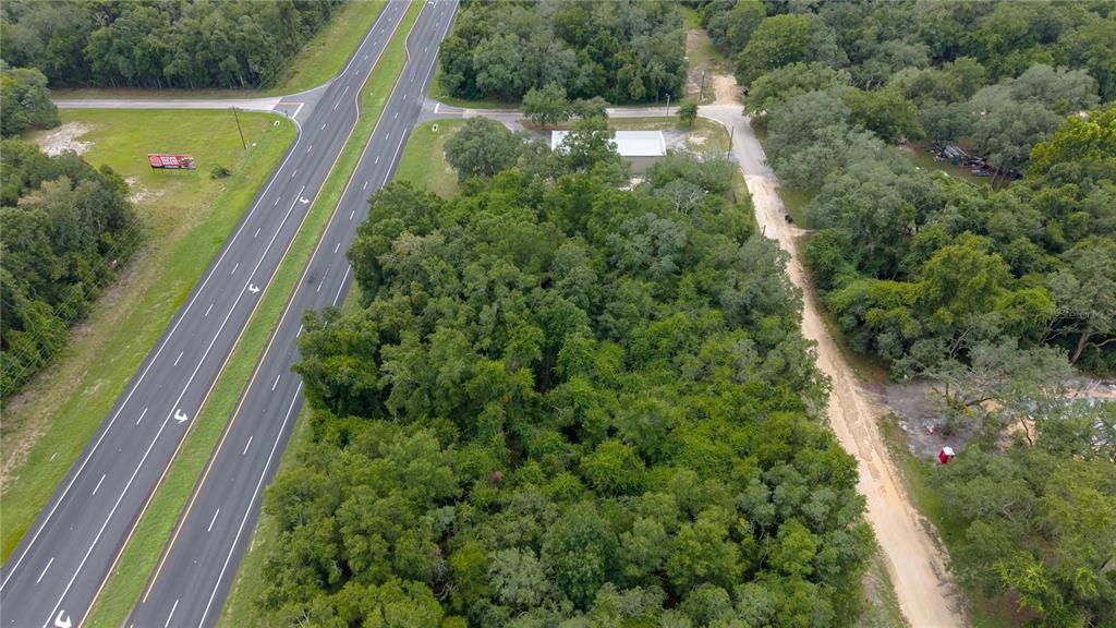 An aerial view shows a wooded lot situated between a highway and a dirt road — 0 N HWY 19, CHIEFLAND, FL